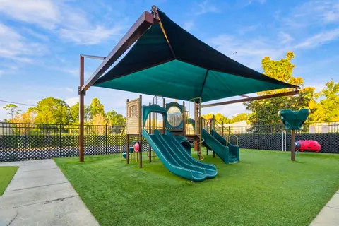 Shaded playground structure with slides and a turf lawn