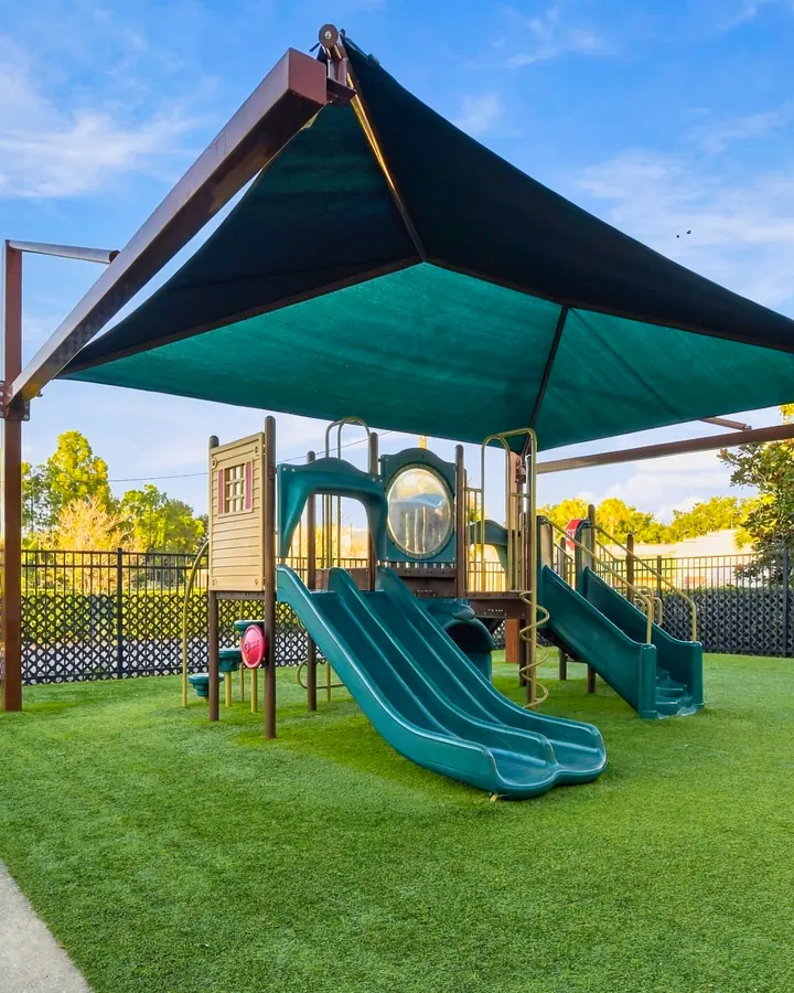 Shaded playground structure with slides and a turf lawn