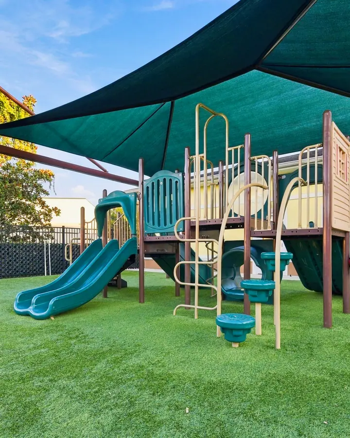 Shaded play structure with slides beside the school building