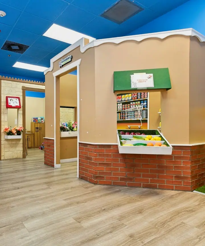 PlayTown street with a pretend grocery stand under a blue sky ceiling