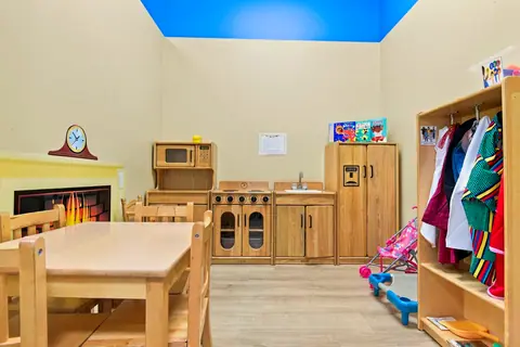 Pretend home corner with a wooden play kitchen, table and dress-up rack