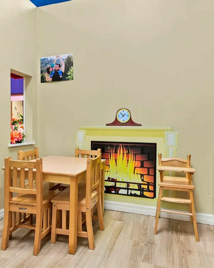 Wooden table and chairs beside a pretend fireplace and play kitchen