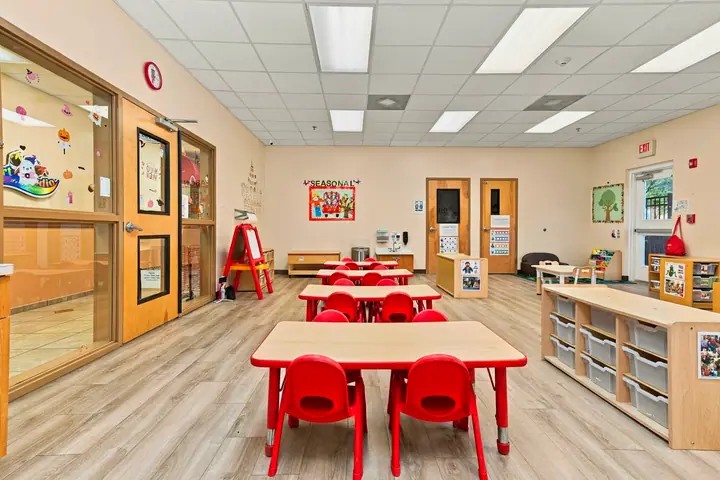 Classroom with red tables, an easel and labeled storage cubbies