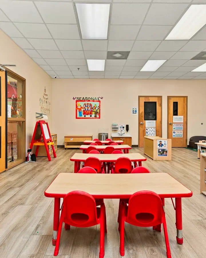 Classroom with red tables, an easel and labeled storage cubbies